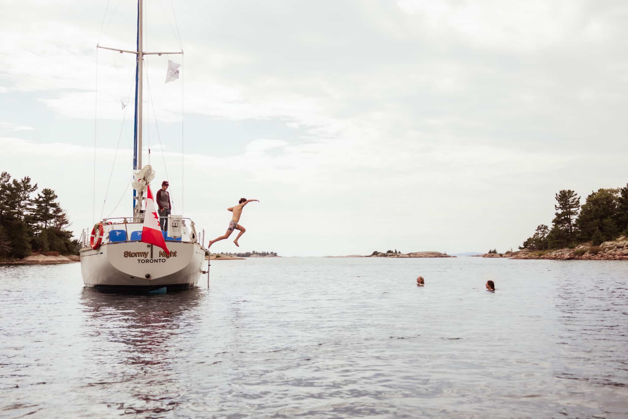 A swimmer leaping from a sailboat anchored in a granite cove on Georgian Bay