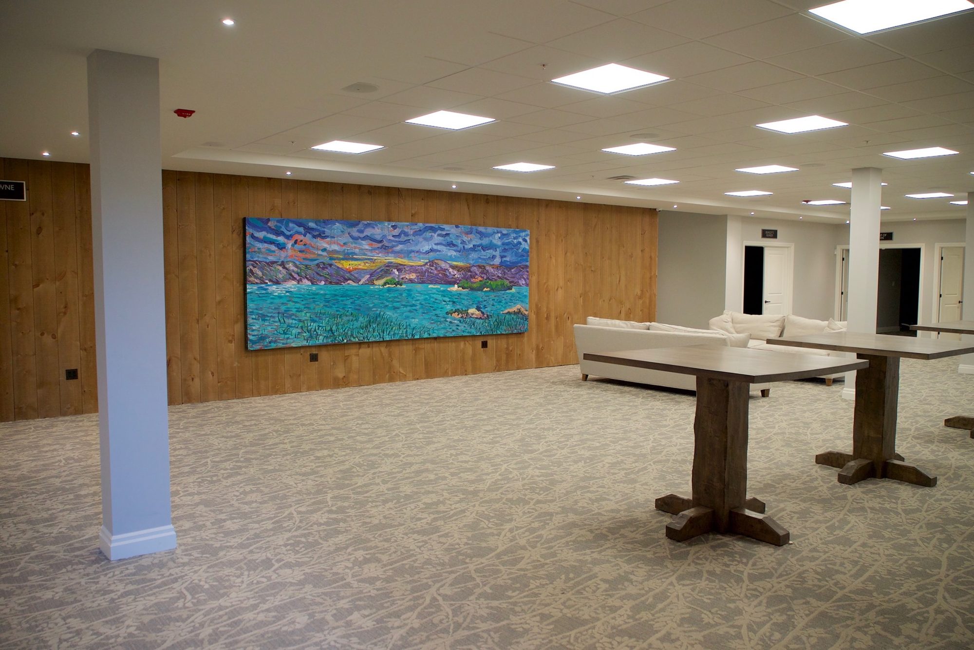 A pre-function reception hall with a wood-plank accent wall and a large abstract lake painting