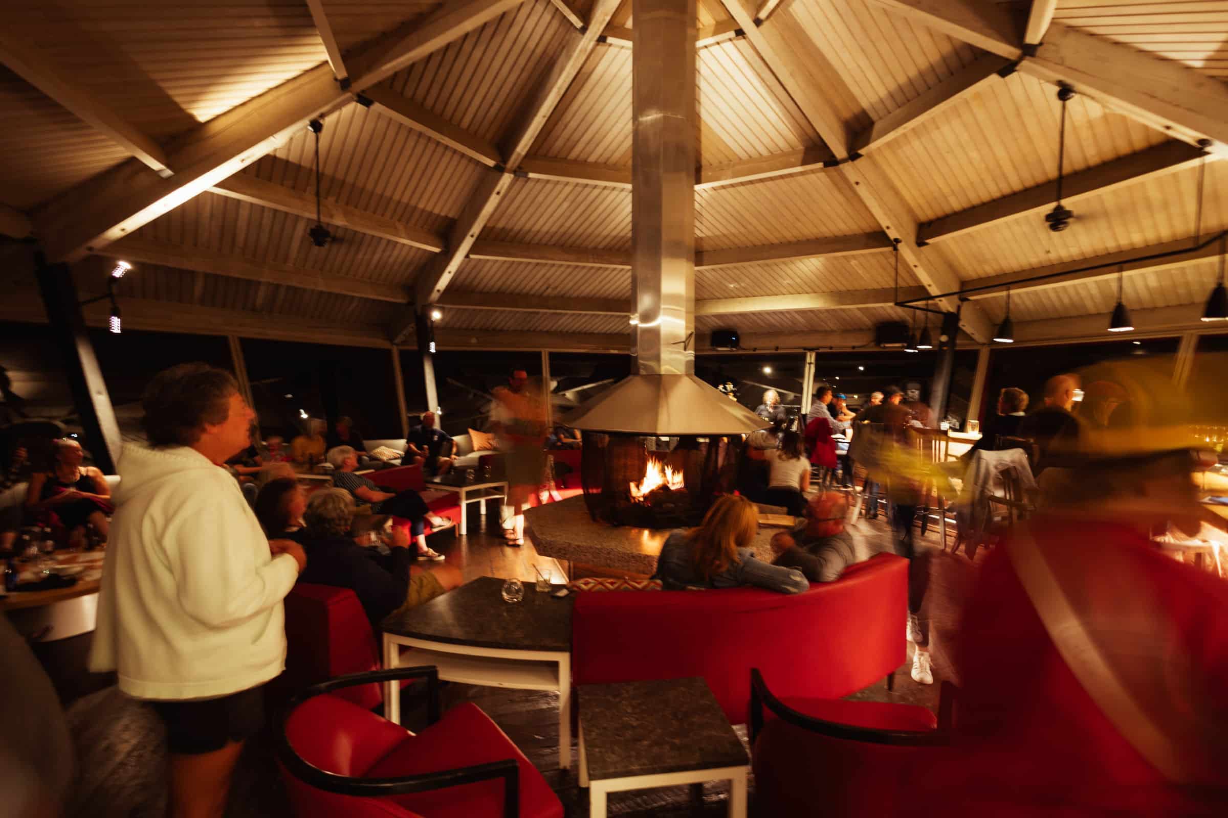 Friends gathered around the open central fireplace of the lounge at night