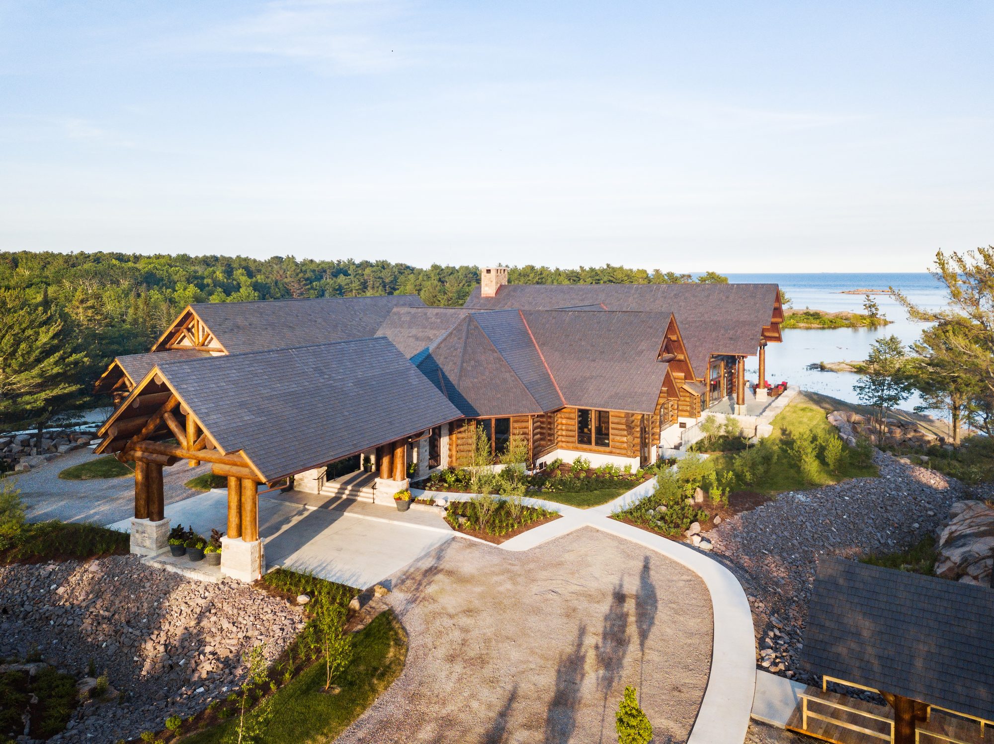 Aerial view of the log porte-cochère entrance at golden hour, the bay beyond