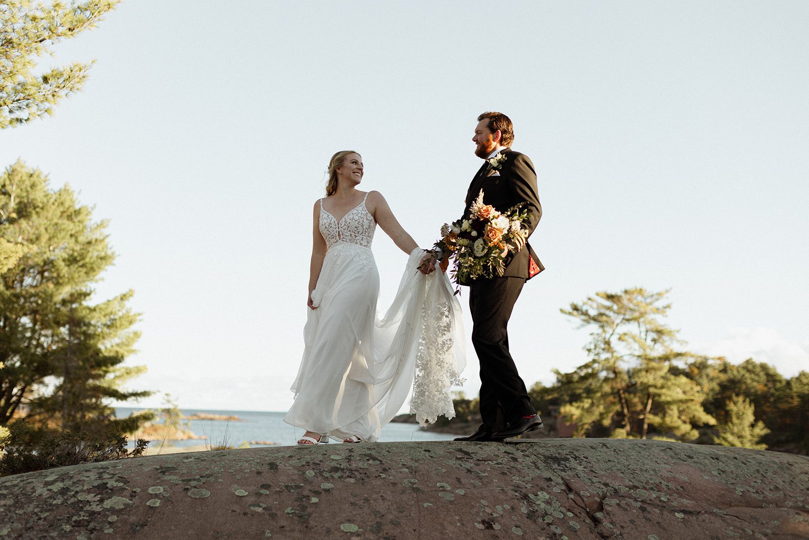 Couple hand in hand on lichen-dotted granite above the bay